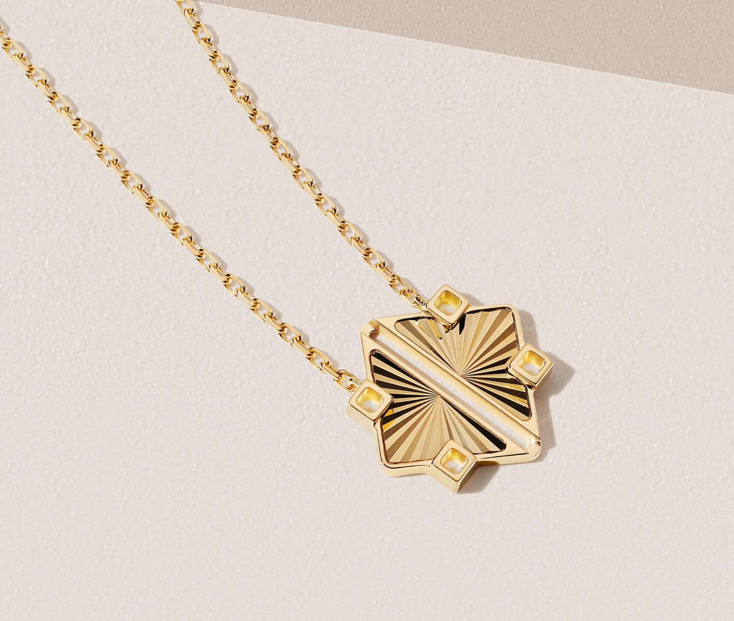 Birks Muse yellow gold pendant on a beige background.